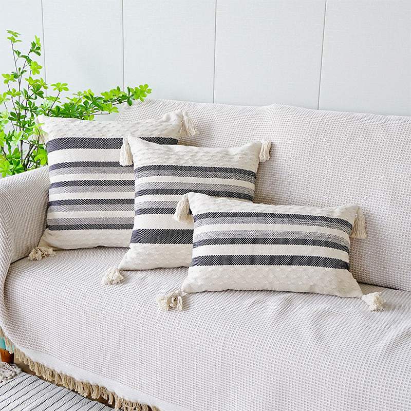black and grey striped cushion with a white background, tassels on each corner and a textured feel on the bottom and top