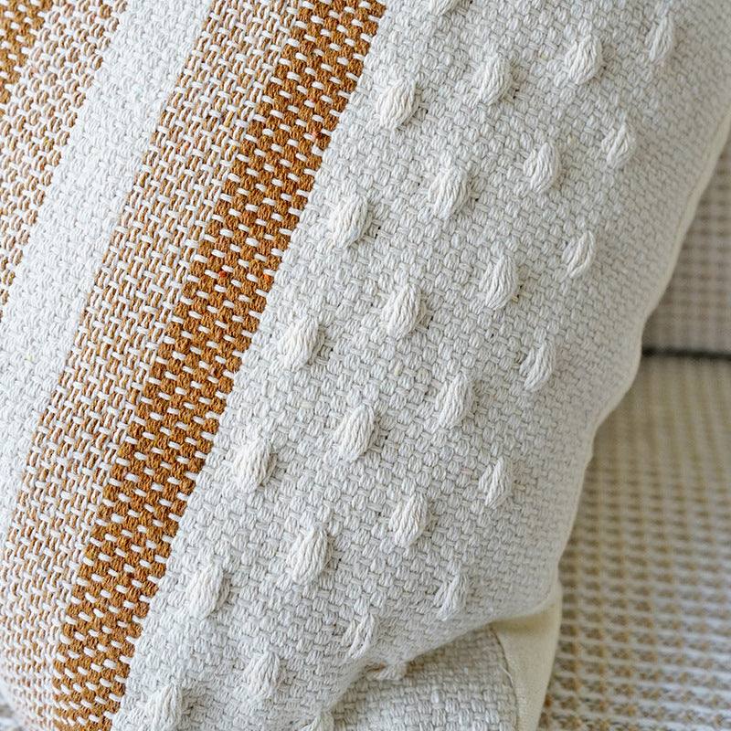 Two shades of brown striped cushion with a white background, tassels on each corner and a textured feel on the bottom and top close up