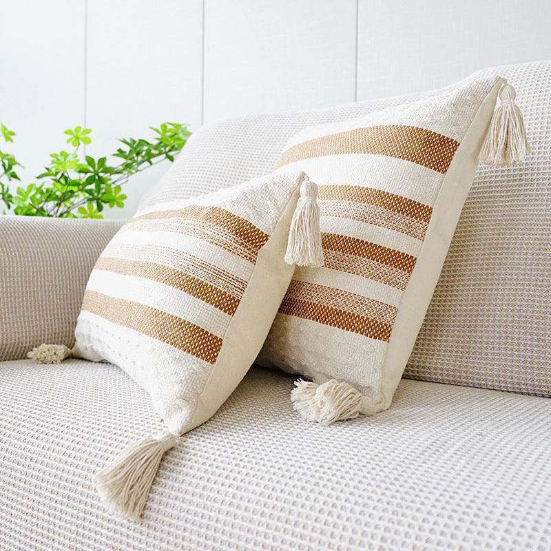 Two shades of brown striped cushion with a white background, tassels on each corner and a textured feel on the bottom and top