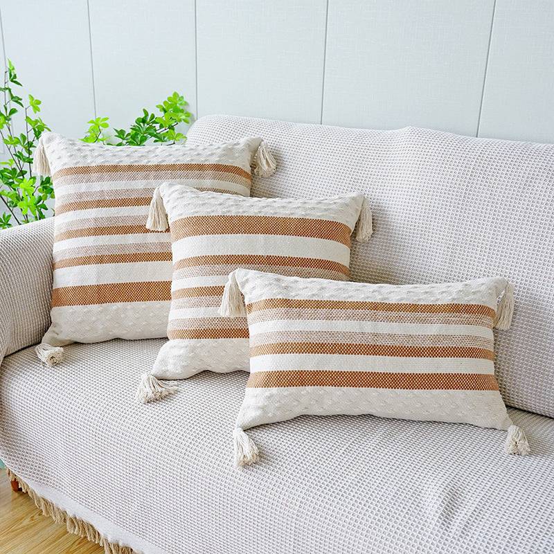 Two shades of brown striped cushion with a white background, tassels on each corner and a textured feel on the bottom and top