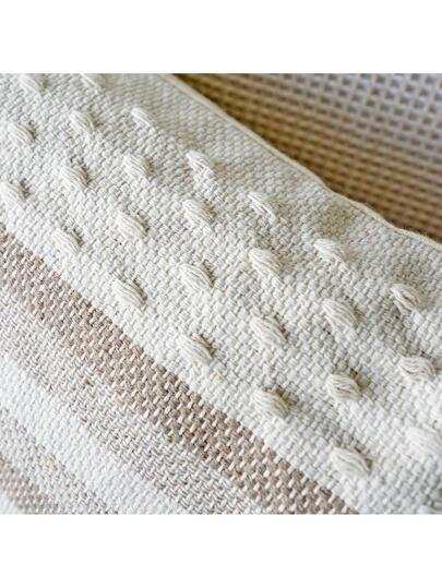 Two shades of khaki striped cushion with a white background, tassels on each corner and a textured feel on the bottom and top close up