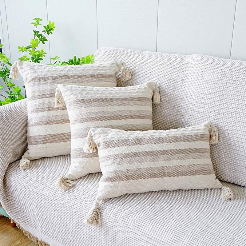 Two shades of khaki striped cushion with a white background, tassels on each corner and a textured feel on the bottom and top